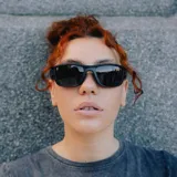 Lentes de sol unisex con marco negro y lentes espejadas polarizadas color celeste. Fabricados con plástico reciclado.