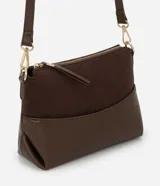 Cartera transversal pequeña color marrón, con la parte superior de gamuza y la inferior de cuero sintético. Tiene cierre de cremallera metálica dorada y asa larga ajustable y desmontable con mosquetones dorados.