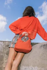 Bolso de nylon color naranja quemado, con textura sutil y manija fruncida. Presenta un parche rectangular negro con el logo 'KUL.' en blanco en el frente.