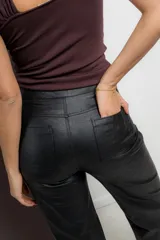 Pantalón de ecocuero negro con textura rústica, corte recto, bolsillos delanteros y traseros funcionales, cierre frontal con botón y cremallera.