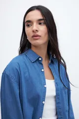 Camisa de denim azul de algodón, con cuello solapa, calce relaxed, manga larga y bolsillo cuadrado en el pecho. Cierre frontal con botones personalizados.