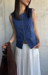 Chaleco de denim azul con escote en V y cierre frontal con botones. Tiene dos bolsillos frontales a la altura de la cintura.