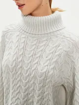 Polerón de tejido de punto color gris claro, con cuello alto y diseño de trenzas en el cuerpo y mangas. Corte holgado y puños anchos.