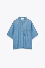 Camisa de denim celeste con cuello solapa, manga corta, bolsillo de parche en el pecho, bajo con aberturas laterales y cierre frontal con botones.