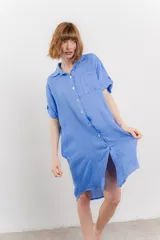 Vestido camisero corto color verde oliva, confeccionado en lino 100%. Tiene botones en la parte delantera, cuello camisero, mangas cortas con botón para arremangar y bolsillos laterales.