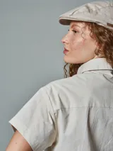 Camisa corta de manga corta, color crudo, con cuello camisero y un bolsillo frontal.