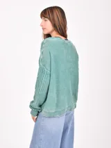 Buzo de tejido de punto color verde menta, con cuello en V y diseño de trenzas en el frente y mangas. Presenta un efecto desgastado o lavado.