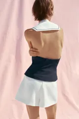 Falda pantalón corta de tiro alto color blanco con detalle de doble fila de botones negros en el frente y cierre lateral con cremallera oculta.