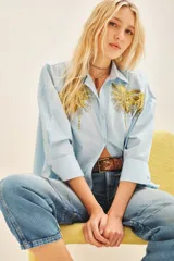 Camisa celeste de poplin con bordados de palmeras doradas en el frente, de corte amplio, con cuello y cartera.