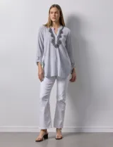 Blusa de gasa bambula a rayas verticales celestes y blancas, con cuello a la base, escote en V con botones y bordado floral negro. Mangas largas regulables con presilla y botón.