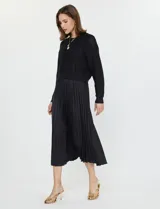 Conjunto de buzo y vestido negro marca Current Air. El vestido es de satén con escote en V y falda plisada. El buzo es de tejido calado, liviano y delicado.