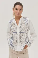 Camisa blanca de lino con bordados florales en tonos beige y azul.