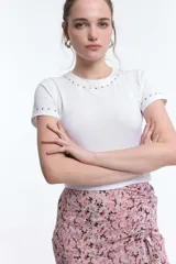 Remera blanca de algodón con cuello redondo y mangas cortas, con detalle de tachas plateadas en cuello y mangas.