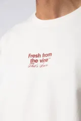 Remera color beige de corte oversize, con cuello redondo y mangas cortas. Estampa pequeña en el frente con la frase "Fresh from the vine".