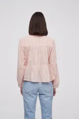 Blusa blanca con rayas verticales, cuello con lazo, mangas largas y corte holgado.