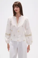 Blusa de algodón color tostado con bordados geométricos en blanco y azul marino, cuello mao con escote en V y mangas largas abullonadas con puños elásticos.
