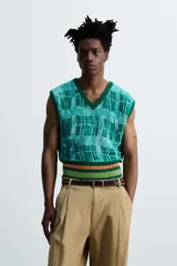 Chaleco cropped de punto con cuello en V, estampado a cuadros en tonos verde y celeste, y ribete inferior a rayas horizontales en verde y naranja.