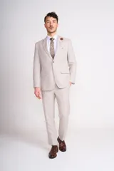 Traje de lino color beige claro, compuesto por saco de dos botones con solapa de muesca, dos bolsillos delanteros con solapa y un bolsillo en el pecho, y pantalón de vestir de corte recto. Incluye camisa blanca, corbata estampada y zapatos marrones.