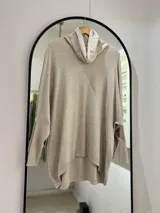 Polerón beige de corte oversize, con cuello drapeado y mangas largas caídas. La parte delantera es más corta que la trasera.