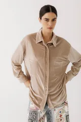 Camisa beige de terciopelo con cuello clásico, cierre frontal con botones, dos bolsillos de parche en el pecho y mangas largas con puños abotonados.