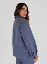 Chaqueta azul de lino con cuello camisero, cierre frontal con botones, mangas largas con puños abotonados, dos bolsillos de parche en el pecho y bajo con terminación desflecada.