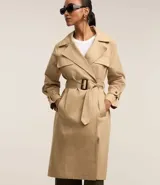 Trench coat largo color beige confeccionado en gabardina de algodón, con cuello solapa, cierre frontal abotonado, cinturón con hebilla, bolsillos laterales y trabillas en los puños.