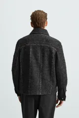 Sobrecamisa negra con textura de tejido bouclé y rayas verticales plateadas. Tiene cuello solapa, manga larga con puños abotonados, bolsillos laterales y cierre frontal con cremallera.