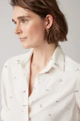 Camisa de lino color blanco hueso con estampado floral en tonos marrones. Tiene cuello clásico, cierre frontal con botones y mangas largas con puños abotonados.