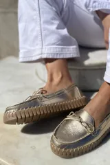 Mocasín náutico dorado de cuero con detalle de lazo en la parte delantera y suela de goma color caramelo.