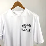 Remera blanca de algodón con estampa en el frente con la frase "CHANGE THE RULES" y un dibujo de una persona. En la parte inferior tiene otra estampa con texto ilegible.