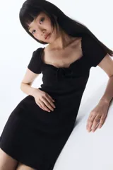Vestido corto negro de punto acanalado con escote corazón ribeteado en encaje y cordón para ajustar en el centro del busto. Modelo de manga corta con cuerpo entallado, copas preformadas y pollera con vuelo.