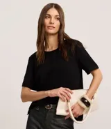 Blusa blanca de poliéster con cuello redondo, mangas cortas, cierre trasero en forma de gota, pequeñas aberturas laterales y acabados en pespuntes en las mangas y el cuello.