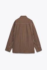 Camisa oversize marrón con rayas verticales blancas, cuello solapa, manga larga con puños y hombros caídos. Tiene un bolsillo de plastrón en el delantero, pinzas en la espalda y cierre frontal con botones.