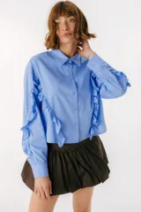 Camisa celeste con cuello clásico, cierre frontal con botones y mangas largas con volados.