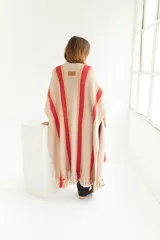 Ruana artesanal color beige con rayas horizontales rojas y amarillas, y flecos en el borde inferior.