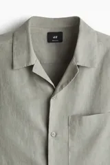 Camisa de manga corta color verde oliva, con cuello cubano, bolsillo de parche en el pecho y cierre frontal con botones. Corte regular fit.