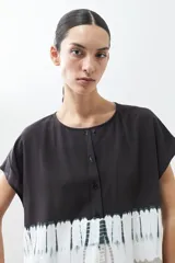 Blusa de manga corta con cuello redondo y cierre frontal parcial con botones. Presenta un diseño tie dye en tonos grises y blancos en la parte inferior.