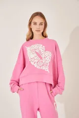 Buzo rosa con cuello redondo y estampado de flores blancas formando un corazón en el frente.