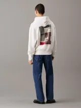 Buzo con capucha confeccionado en felpa de algodón regenerativo color blanco. Tiene corte relaxed, capucha con cordón, puños y bajo de canalé, logo bordado en el bajo en el mismo tono y estampado fotográfico digital de Calvin Klein en la parte trasera.