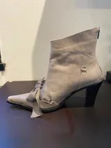 Bota de cuero color gris topo con punta fina, taco bloque negro y lazo decorativo en el empeine.