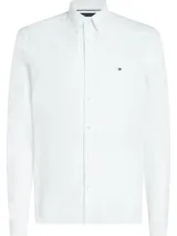 Camisa blanca de corte regular, confeccionada en tejido Oxford Dobby de mezcla de algodón. Tiene cuello abotonado, cierre con botones, manga larga y logo de Tommy Hilfiger bordado en el pecho.