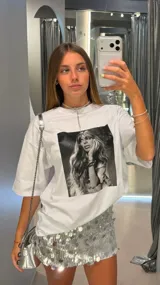 Remera blanca de algodón, corte oversize, con estampa fotográfica en blanco y negro de una mujer con cabello largo y accesorios.
