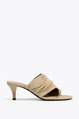 Sandalia color beige de ante, estilo mule, con tira ancha arrugada y posición para el dedo. Tacón fino medio y acabado en punta redonda.