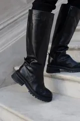 Bota alta de cuero color negro con puntera marrón, caña alta y suela track.