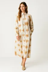 Vestido camisero midi de manga larga, color crudo con estampado tie-dye en tonos marrones. Tiene cuello camisero, abotonadura frontal completa y corte holgado.