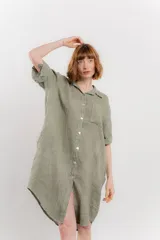Vestido camisero corto color verde oliva, confeccionado en lino 100%. Tiene botones en la parte delantera, cuello camisero, mangas cortas con botón para arremangar y bolsillos laterales.