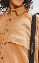 Camisa manga corta color beige, con cuello clásico, cierre frontal con botones, doble bolsillo con ojal en el delantero y silueta oversize.