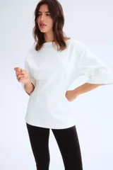 Remera larga color blanco de punto pesado de algodón, con escote barco, hombros caídos, mangas al codo y cintura entallada con pinzas acolchadas.