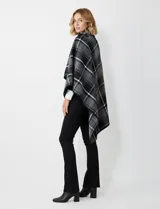 Capa corta de tejido grueso, color verde esmeralda con diseño de cuadros escoceses en azul marino y líneas finas en beige. Posee cuello alto que se cruza al frente y se cierra con un broche oscuro.