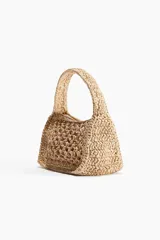 Cartera de mano color beige, confeccionada en paja trenzada de papel. Tiene asa corta y cierre superior con cremallera.